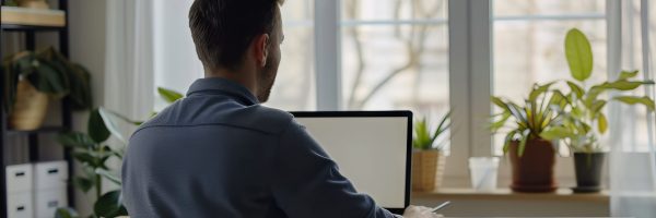 person-sitting-desk-with-computer-surrounded-by-houseplants-furniture-vase-flowers-front-window